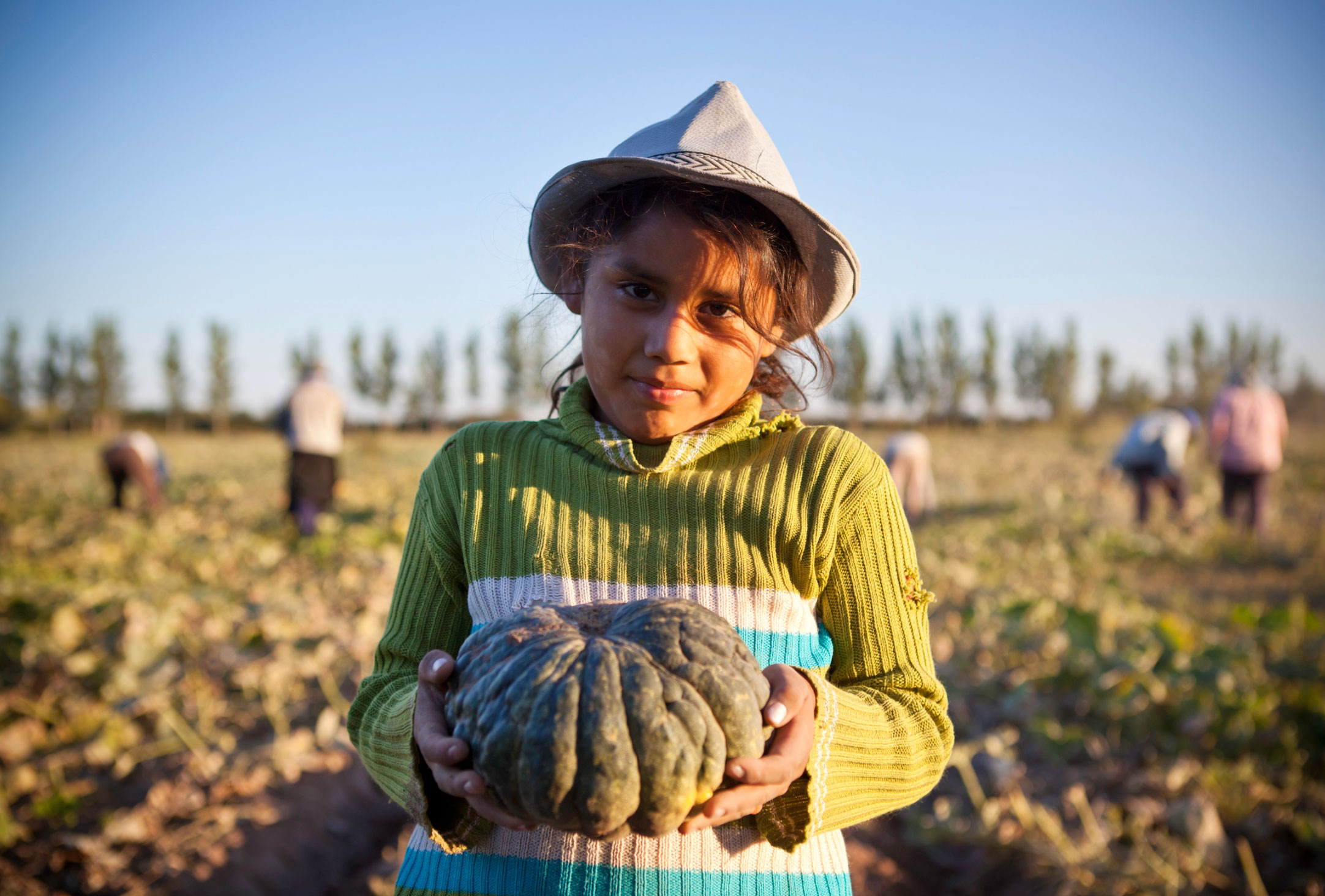 A child working in a field holding produce for the camera.