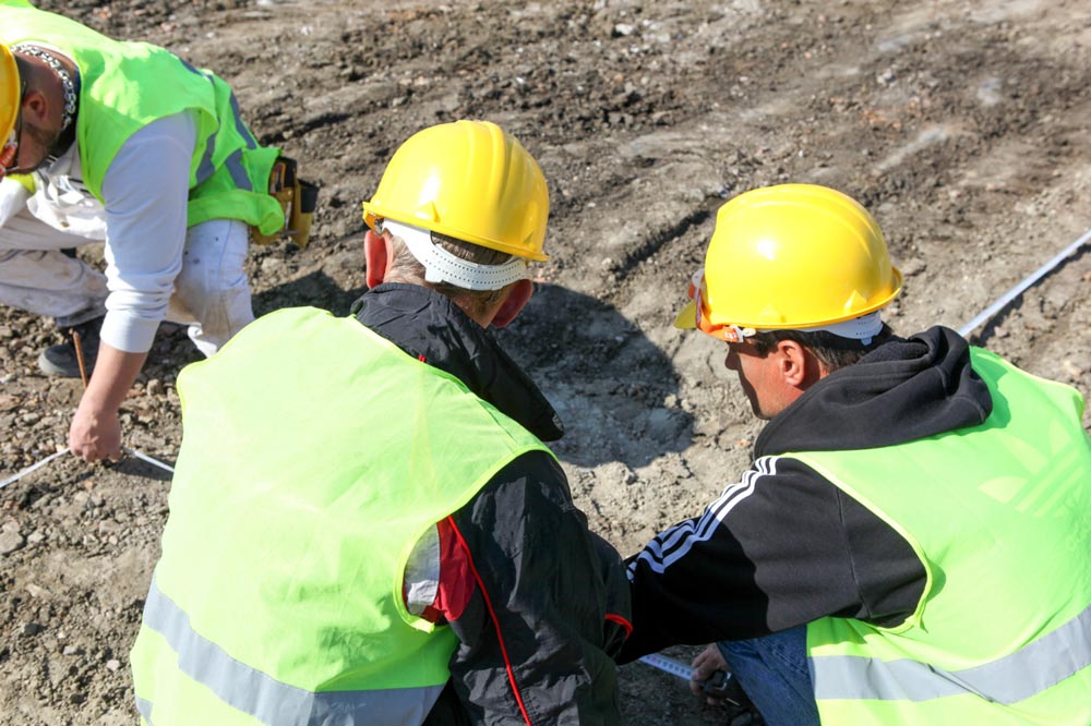 People in hard hats and high vis vests looking at dirt.